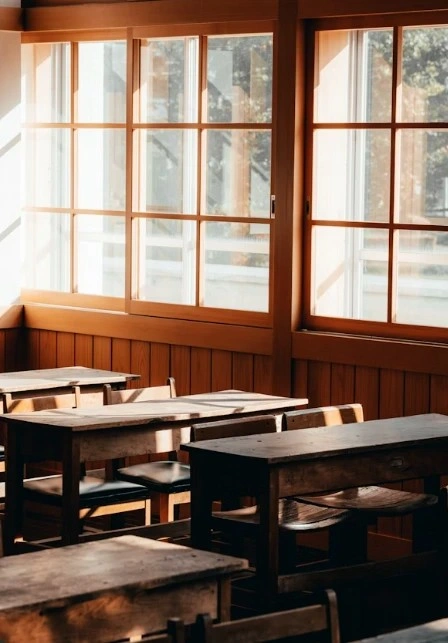 Vintage classroom with wooden desks and large sunlit windows creating a warm learning environment.